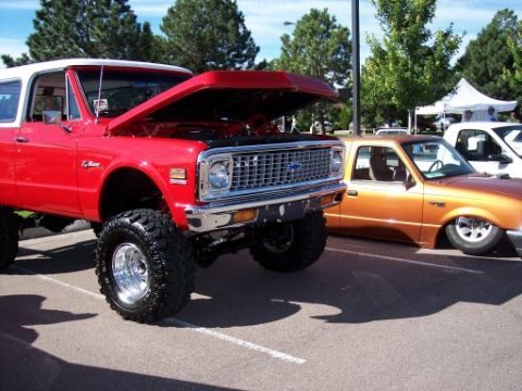 1972 Ford Ranchero - A red and white lifted SUV is parked next to an orange pickup truck at a car show.