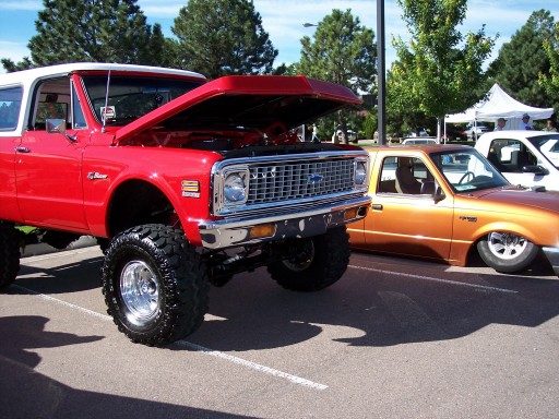 Red and white lifted SUV with hood open, front grille visible. Orange pickup truck in background