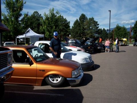 1972 Ford Ranchero - Several vehicles are parked in a lot under a sunny sky, with trees and mountains in the background.