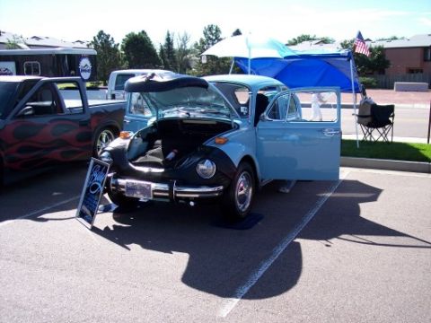 1972 Ford Ranchero - A light blue Volkswagen Beetle is displayed with its hood and door open at a car show, parked next to a pickup truck.