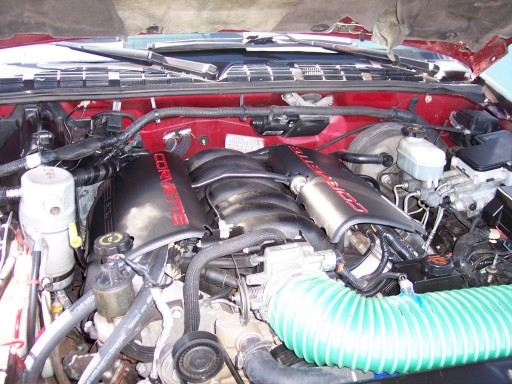 Engine bay showing black valve covers with red 'CORVETTE' lettering and a green ribbed intake hose