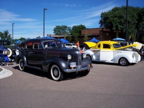1972 Ford Ranchero - A dark gray sedan with red pinstripes and whitewall tires is parked at a car show next to a yellow and white coupe.