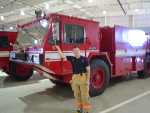 1981 Ford Bronco - A firefighter poses in front of a large red fire truck inside a building.
