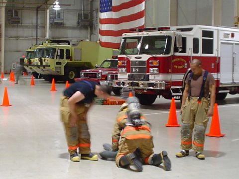 1981 Ford Bronco - Firefighters train in a hangar with multiple emergency vehicles and an American flag overhead.