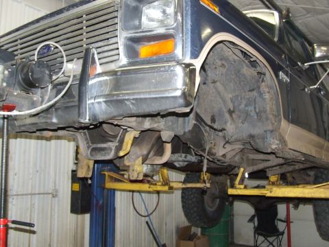 1986 Ford Bronco - The front end of a Ford Bronco is shown raised on a vehicle lift in a garage.