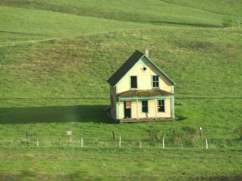 1990 Ford Bronco - An old, weathered house stands alone on a vast, green landscape, its windows dark and empty.