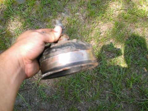 1986 Ford Bronco - A hand holds a rusty, metallic automotive part against a grassy background. The part appears to be a component like a brake drum or hub.