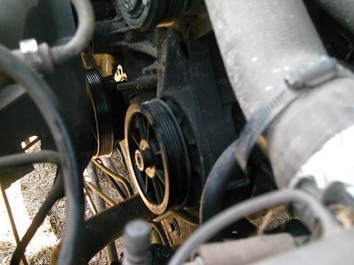 Close-up of engine pulleys and hoses, some are ribbed and black, others are gray and ribbed with a metal clamp