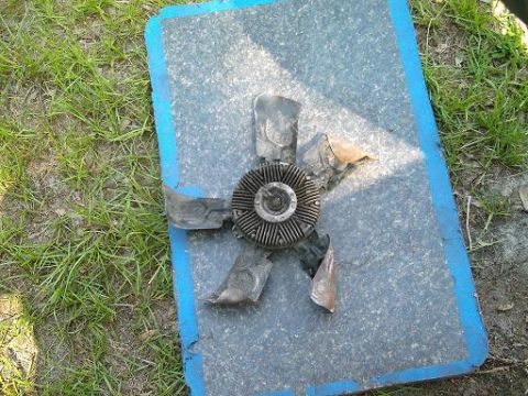 1986 Ford Bronco - A damaged engine cooling fan with bent blades is shown resting on a mat outside.