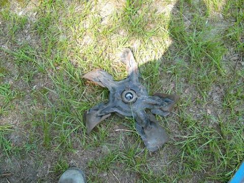 1986 Ford Bronco - A detached fan blade rests on the grass, its metal blades bent and worn.