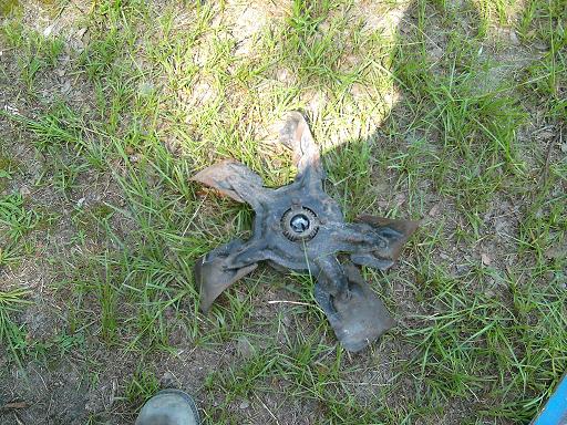 Fan blade with four bent metal blades and a central bearing, lying on grass
