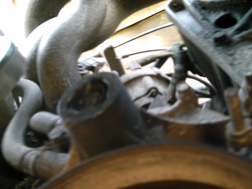 Close-up of engine bay showing various hoses and metal components. A black rubber hose end is prominent in the foreground