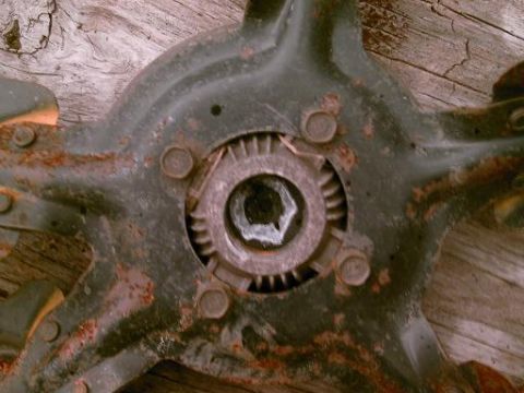 1986 Ford Bronco - Close-up of a heavily rusted metal component, possibly from a vehicle, showing a hexagonal bolt head and surrounding gear-like teeth.