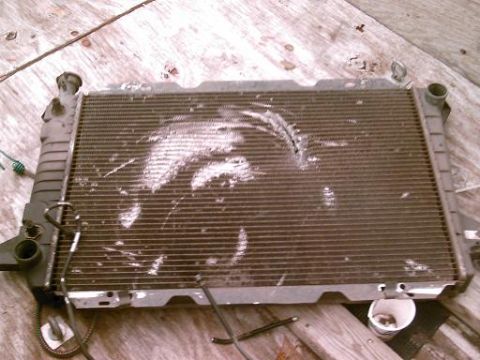 1986 Ford Bronco - A damaged radiator, likely from a vehicle, lies on a weathered wooden surface.