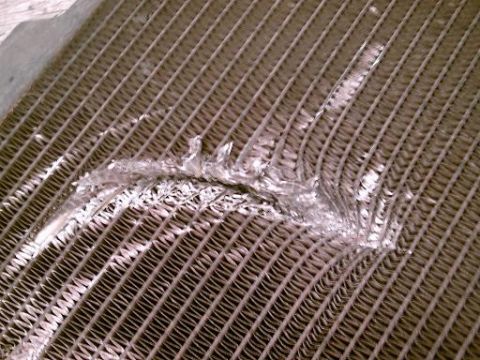 1986 Ford Bronco - Close-up of a damaged radiator, showing bent fins and dried coolant residue.