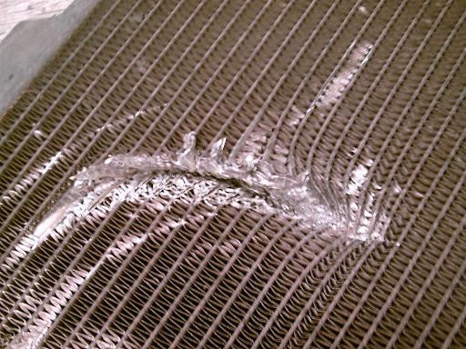 Damaged radiator fins with bent metal and coolant residue