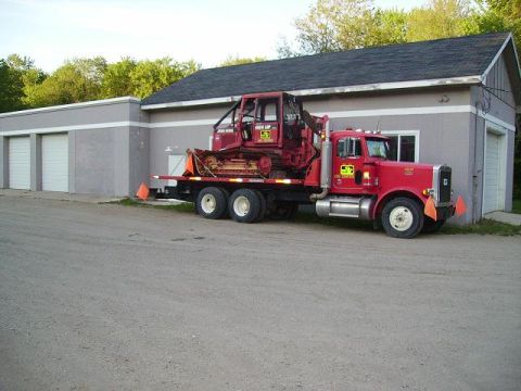 2000 Chevrolet Tahoe - A red semi-truck transports a bulldozer, parked beside a building with multiple garage doors.