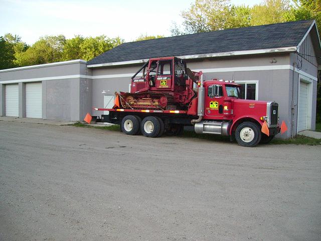 Red semi-truck with a bulldozer on its flatbed parked in front of a garage
