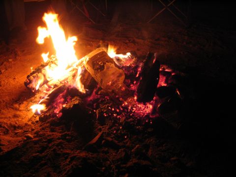 1993 Toyota 4Runner - A campfire burns brightly at night, with logs and a plastic bottle visible in the flames and embers.