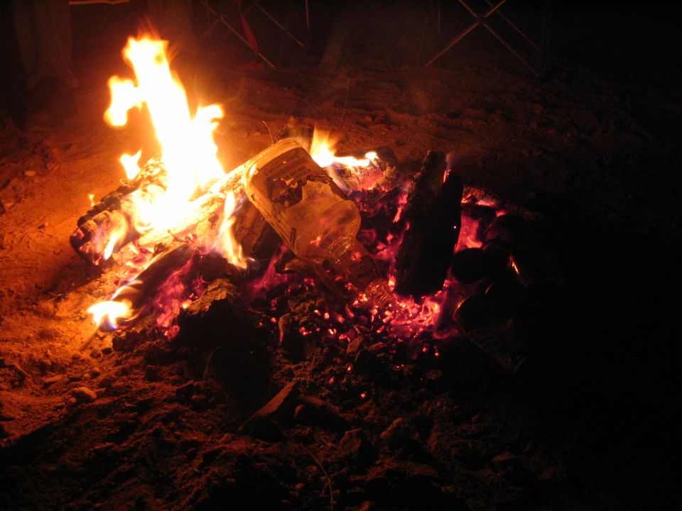 Campfire burning logs and coals in a dirt fire ring at night