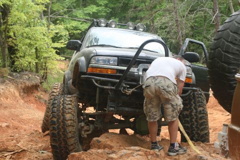 1990 Ford Bronco - A person works on a heavily modified pickup truck during an off-road excursion on a dirt path.
