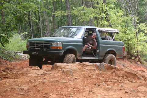 1990 Ford Bronco - A green 1990 Ford Bronco navigates a challenging rocky terrain with a driver visible inside.