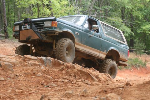 1990 Ford Bronco - 1990 Ford Bronco navigating a challenging off-road trail with large tires and a winch.