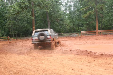 1990 Ford Bronco - A Ford Bronco navigates a muddy off-road course with trees in the background.