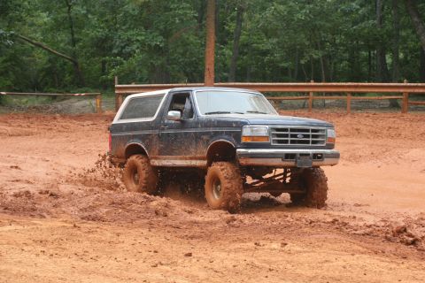 1990 Ford Bronco - This 1990 Ford Bronco is shown off-road, navigating through a muddy terrain with its lifted suspension.