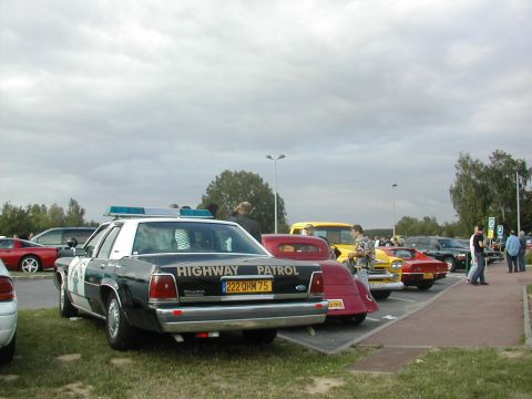 1991 Ford Crown Victoria - A police car is parked in a lot with several other vehicles under a cloudy sky.