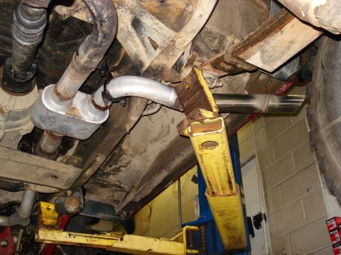 1994 Ford Bronco - Underside view of a vehicle's exhaust system, including muffler and catalytic converter, undergoing maintenance.
