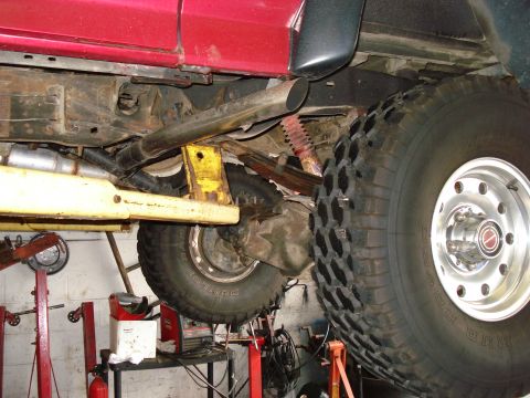 1994 Ford Bronco - The undercarriage of a red vehicle is shown while it is raised on a lift for service.