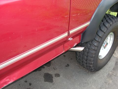1994 Ford Bronco - Close-up view of the side of a red SUV, highlighting the chrome trim, fender flare, and exhaust pipe.