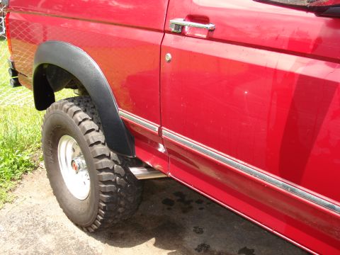 1994 Ford Bronco - Close-up view of a red SUV's side, showing the fender flare and a large tire.