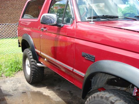 1994 Ford Bronco - Side profile of a red 1994 Ford Bronco XLT, chrome accents and prominent fender flares.
