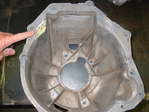 1993 Ford Taurus - A person's finger points to a damaged section of a metal transmission bell housing.