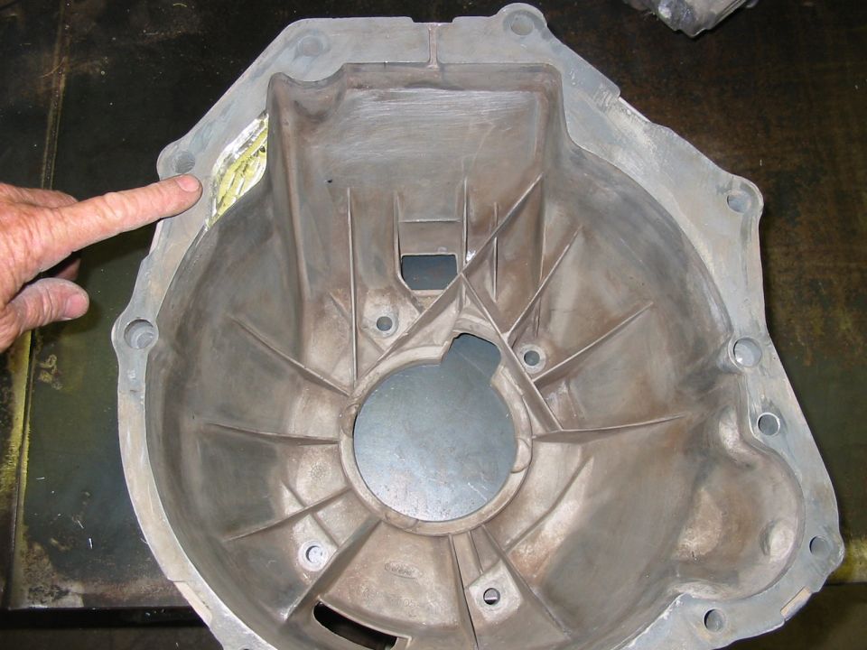 Close-up of a metal transmission bell housing with a finger pointing to a damaged area