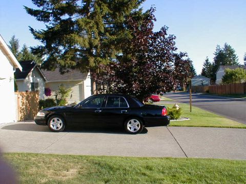 2002 Ford Crown Victoria - A black sedan is parked on a concrete driveway in front of a house on a sunny day.