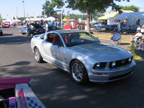 1989 Ford Mustang - A silver 2005 Ford Mustang GT is seen at an outdoor event with tents and other vehicles.