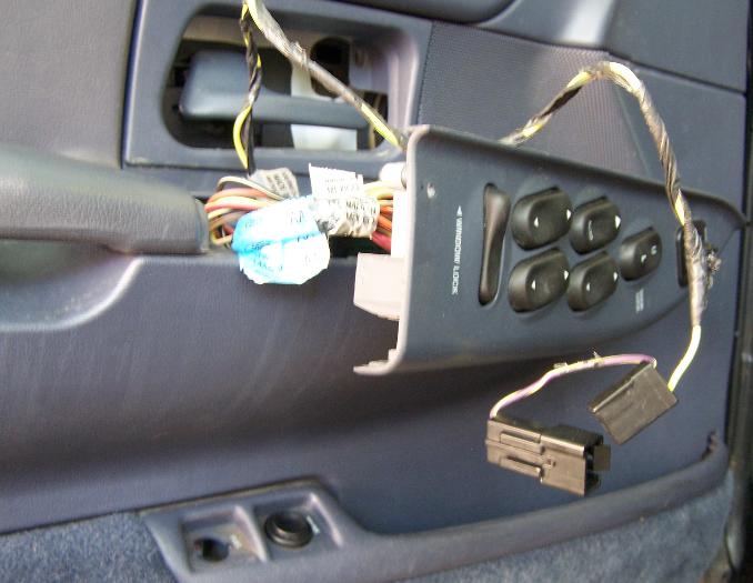 Driver's door master window switch removed and dangling by wires from a blue interior door panel