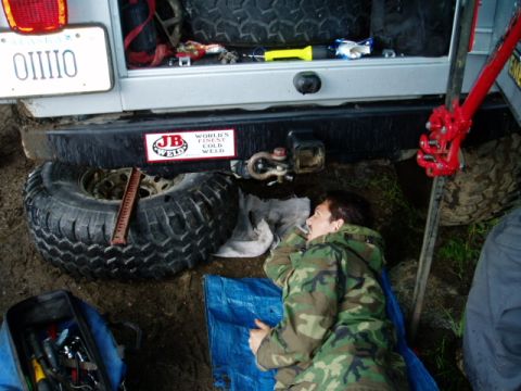 2000 Ford E350 - Person resting on tarp next to spare tire and jack, with vehicle in background.