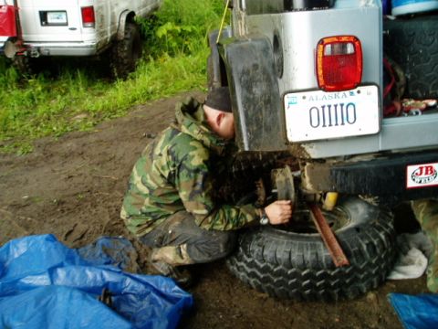 2000 Ford E350 - A person in camouflage works on the rear of a Jeep Wrangler, with a white van visible in the background.