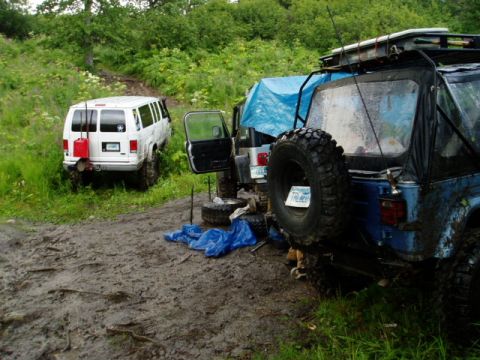 2000 Ford E350 - Two off-road vehicles are parked in a muddy area with trees and foliage in the background.
