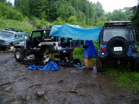 2000 Ford E350 - Two Jeeps and a blue SUV are parked in a muddy, wooded area, with a tarp set up between the Jeeps.