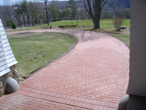 1998 Ford Taurus - A paved brick driveway leads up to a house, surrounded by a green lawn and trees.
