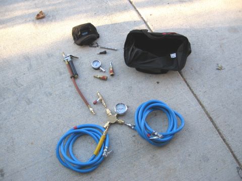 1994 Ford Bronco - A collection of air hoses and tire gauges are spread across a concrete surface next to a black tool bag.