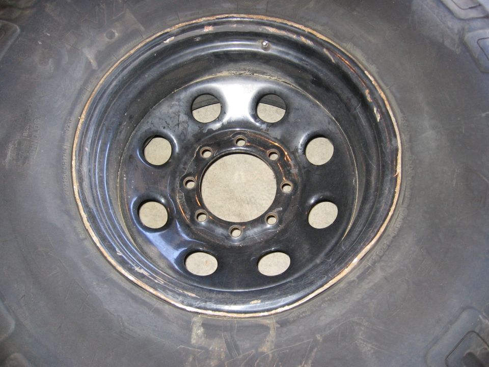 Black eight-slot steel wheel on an off-road tire with chipped paint and no center cap