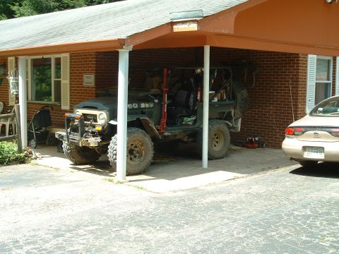 1995 Ford Bronco - An off-road vehicle with prominent tires is parked under a carport next to another car.