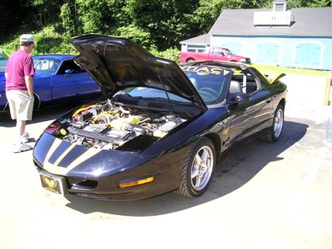 1984 Pontiac Fiero - A black 1994 Pontiac Firebird with yellow racing stripes is parked outside with its hood open, revealing the engine bay.