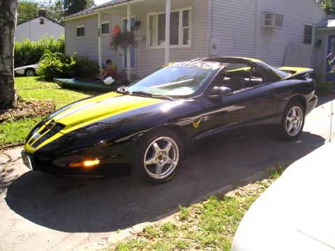 1984 Pontiac Fiero - A black 1994 Pontiac Trans Am with yellow racing stripes is parked in front of a house.